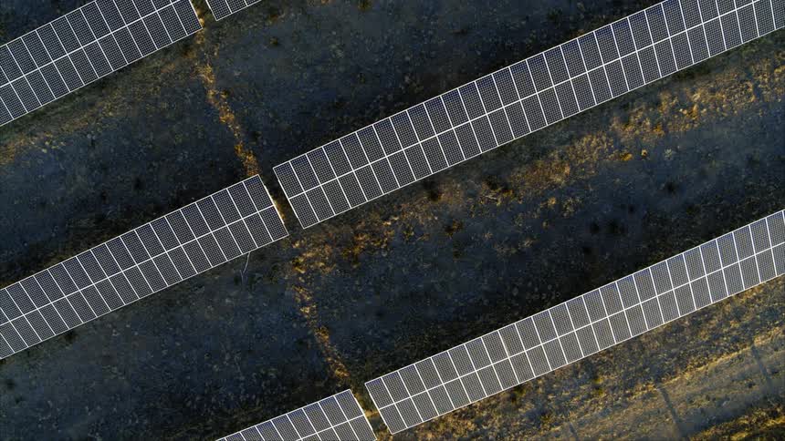 Top down medium shot of double tall solar panel rows bathed in early morning light