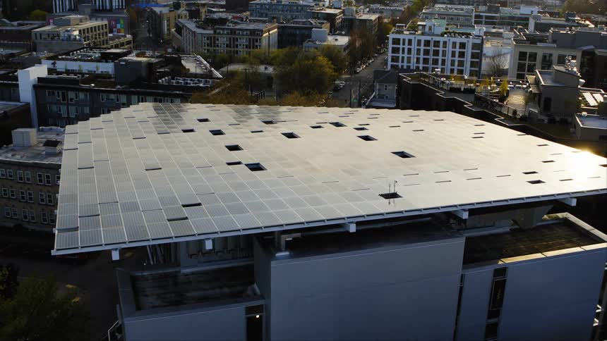 Pullback ascent above a solar panel structure to reveal it is actually the roof of a modern office building in a large city