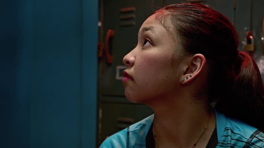 A woman sitting in a locker room with lockers and locks in the background