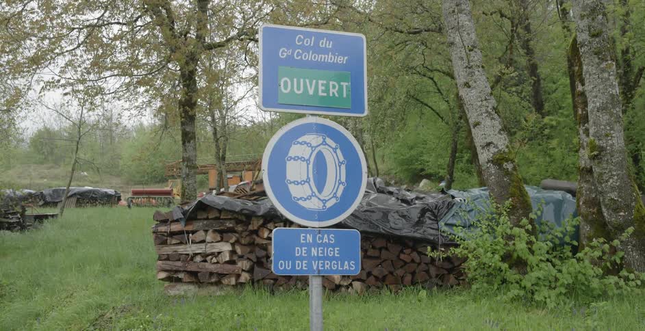 A road sign with a pile of logs behind it