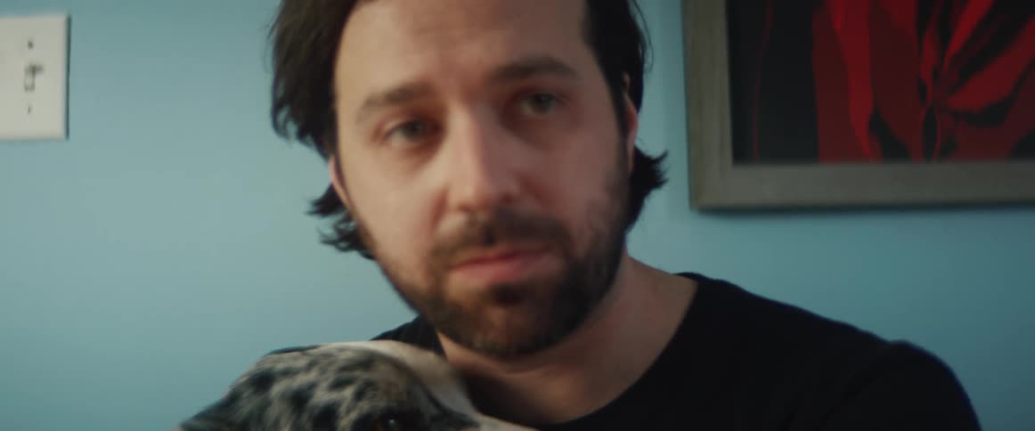 A man in a room with a wristwatch holding a dog with a wall in the background