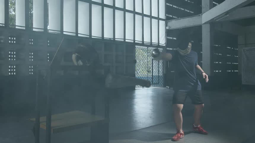 Man practices fencing alone in room filling with dark smoke near wall with windows showing trees outside
