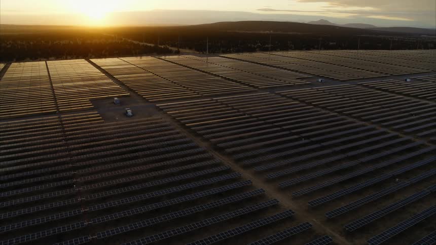 Golden light softy reflects from the panels of a large solar power facility as the sun sets along the horizon