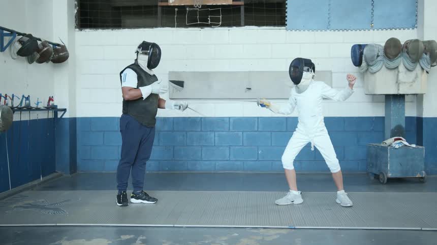 Two people are practicing fencing in the gym