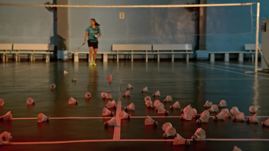 A female athlete is practicing her serve at a badminton court