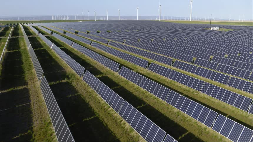 Rows of solar panels aligned in front of wind turbines at a massive green energy facility