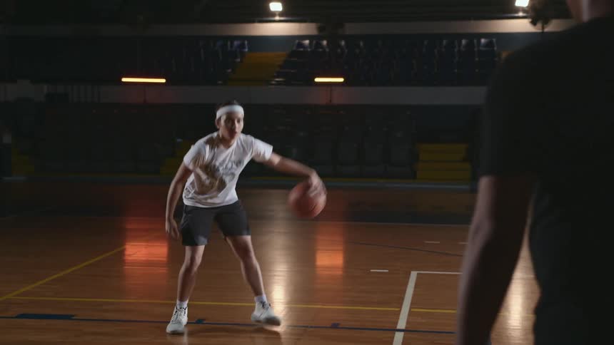 A young male athlete is performing basketball drills with his coach in a gymnasium
