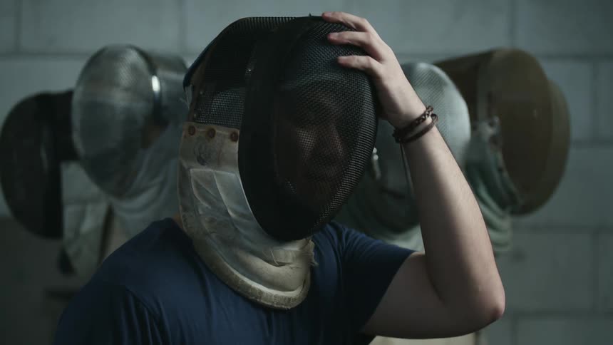 Young man puts on a fencing mask and adopts a stance