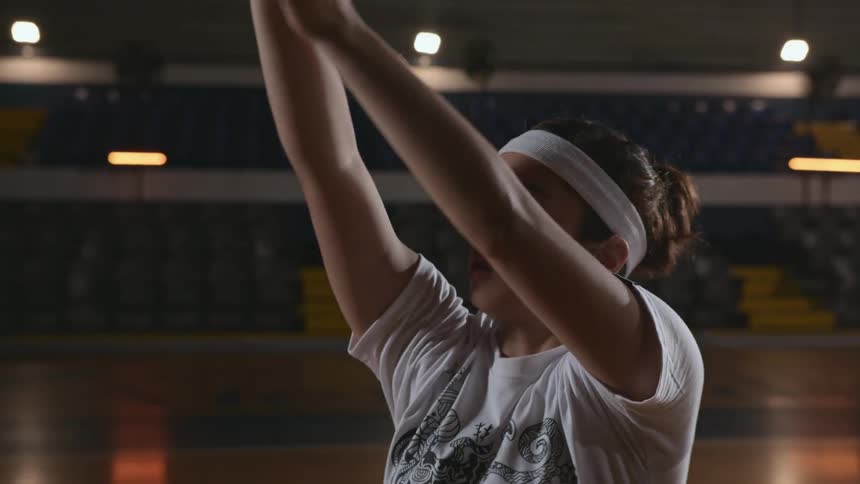 Teenager practices taking basketball shots on empty interior basketball court
