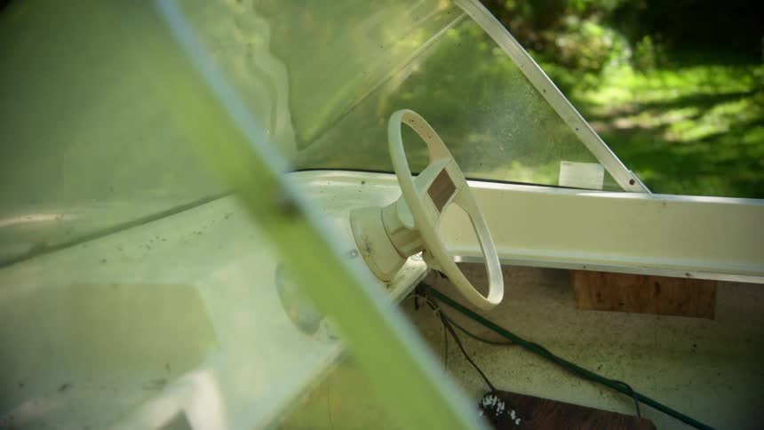 A white steering wheel on a boat parked next to a forest