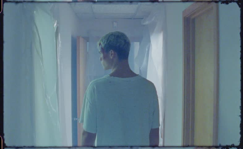 Man with blood on his head walking on a hallway under flashing lights