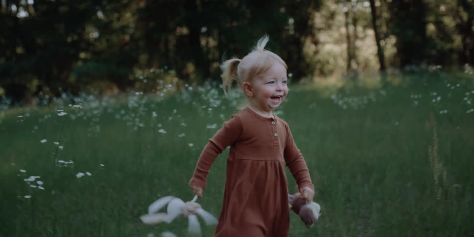 A little girl runs through a field carrying stuffed animals and laughing