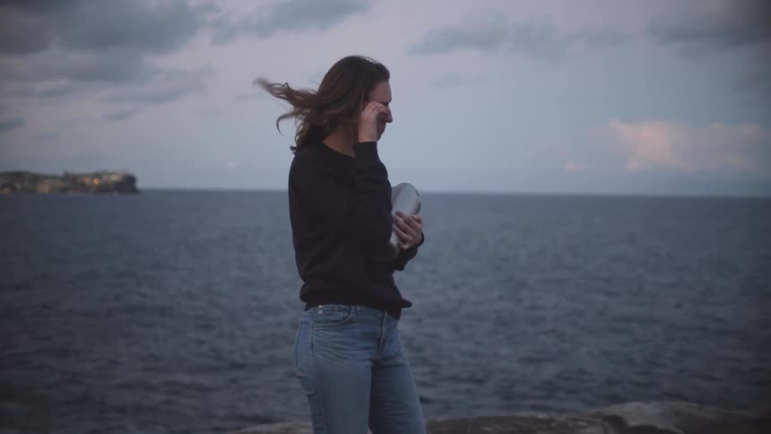 A woman cries while holding an urn by the shore