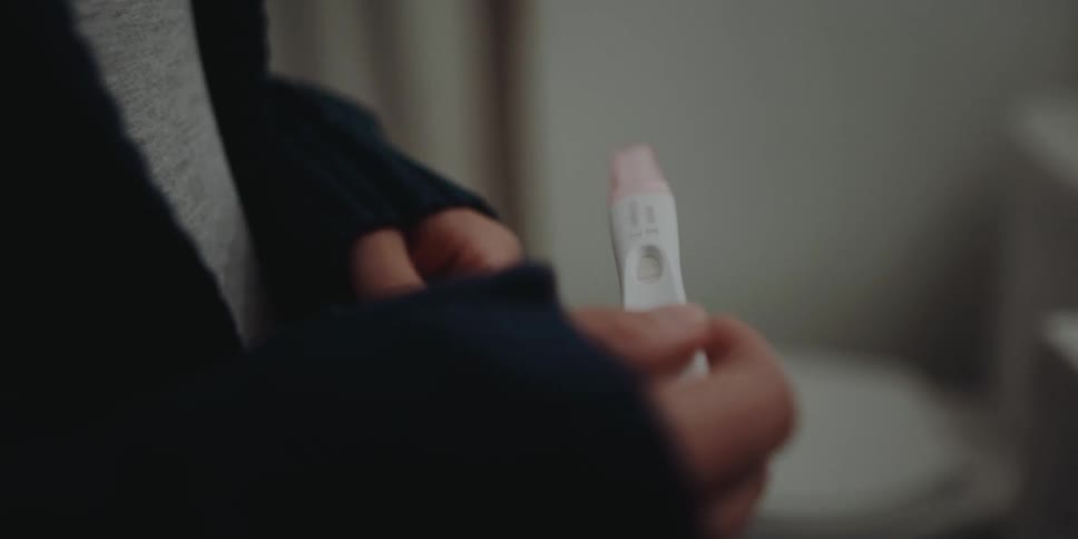 A woman inspects a pregnancy test result while standing in a bathroom