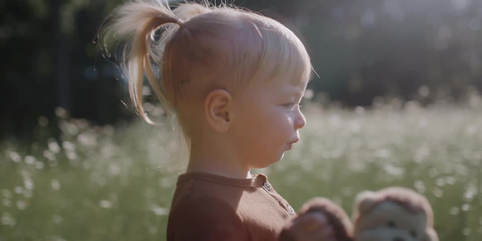 Blonde girl carrying stuffed monkey toy walks through field