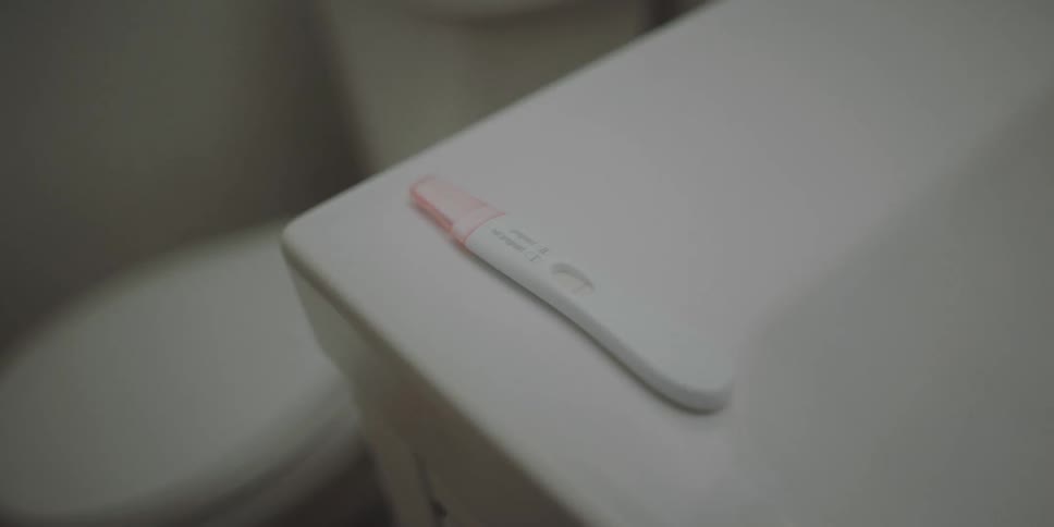 A pregnancy testing stick sits on the counter of a bathroom sink
