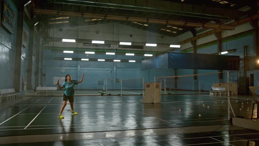 A female plays badminton by herself in a large gym