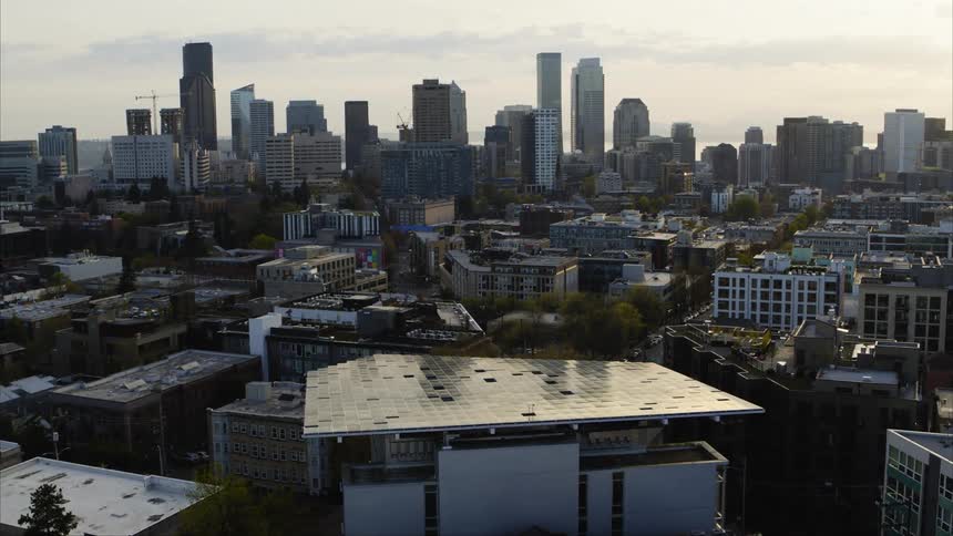 A city skyline is partially reflected in the gleaming solar panels that make up the roof of a LEED certified green building