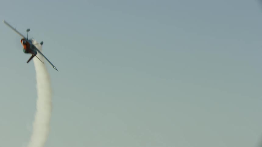 An acrobatic airplane performs a barrel roll with smoke very close to the camera in the sky