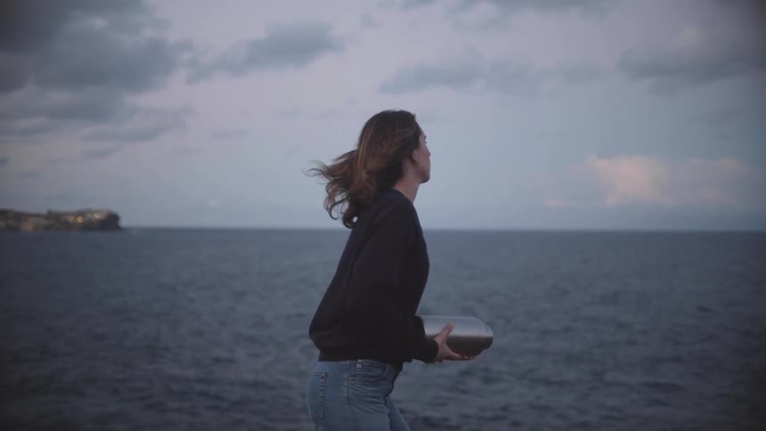 A woman hugs a silver urn to her face then proceeds to throw the ashes into the ocean next to her