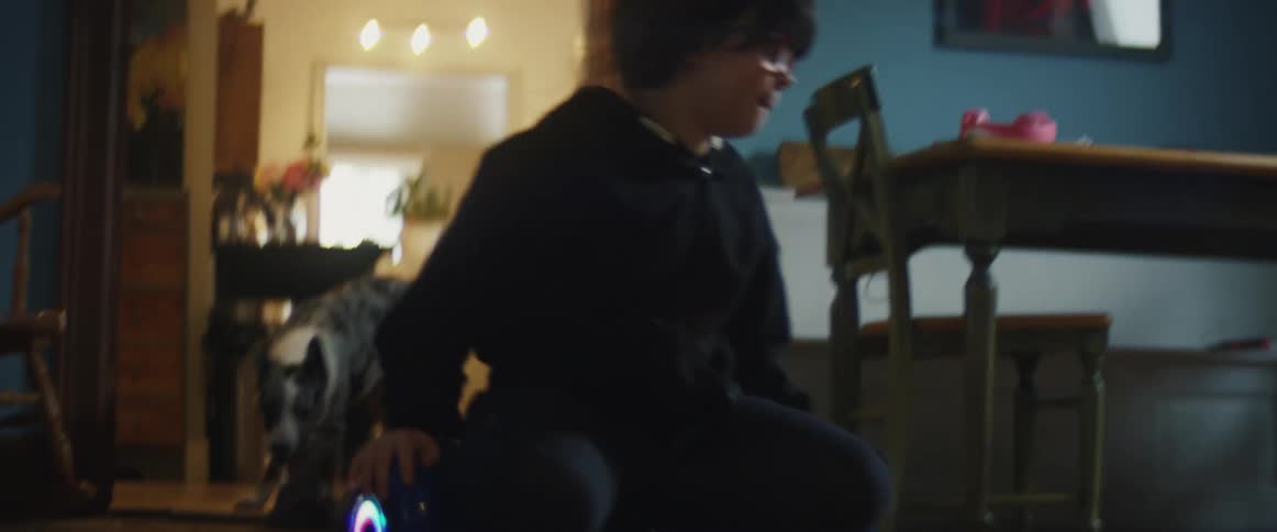 A child kneels on a hover board and does circles in a home living area