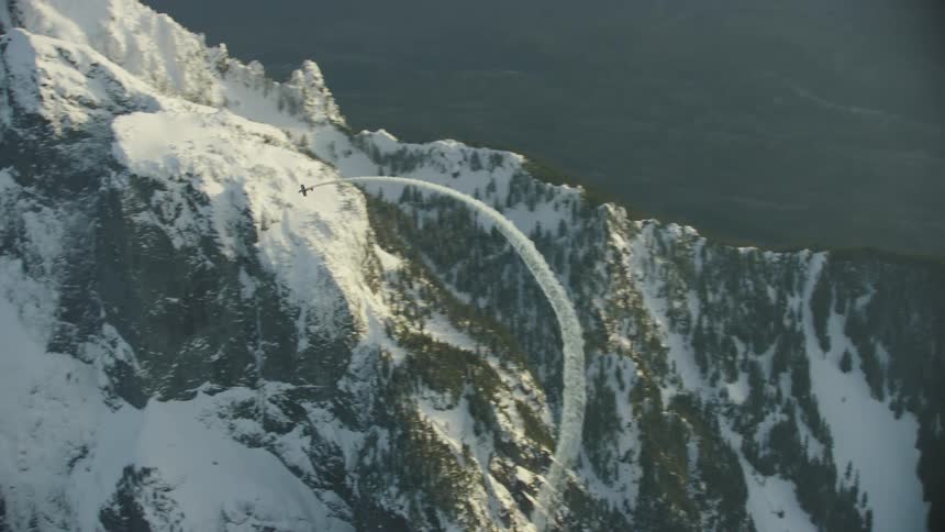 Single engine acrobatic airplane makes a huge loop while the camera tilts down to the valley below