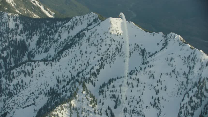A single engine airplane climbs straight up at the camera performs and loop and dives back into the valley in dramatic winter snow covered mountains