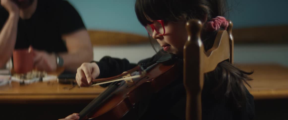 A father is watching his daughter play the violin indoors