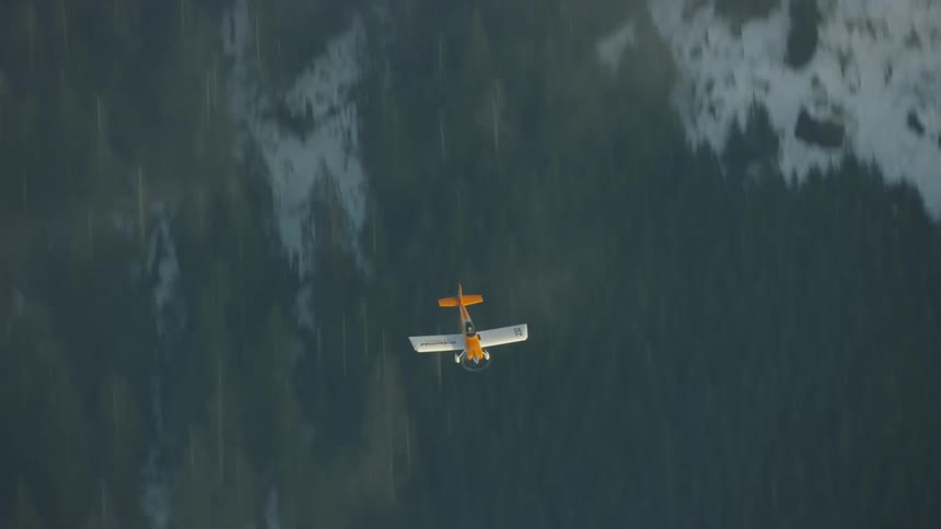 Airplane flies down quickly past snow covered mountain forest skimming through thin clouds in a shot that feels very fast and urgent