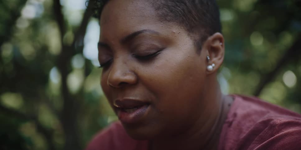 A woman talks out loud while meditating outside near large trees