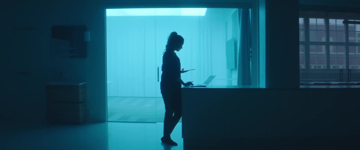 A woman is standing in an empty room and looking at a laptop