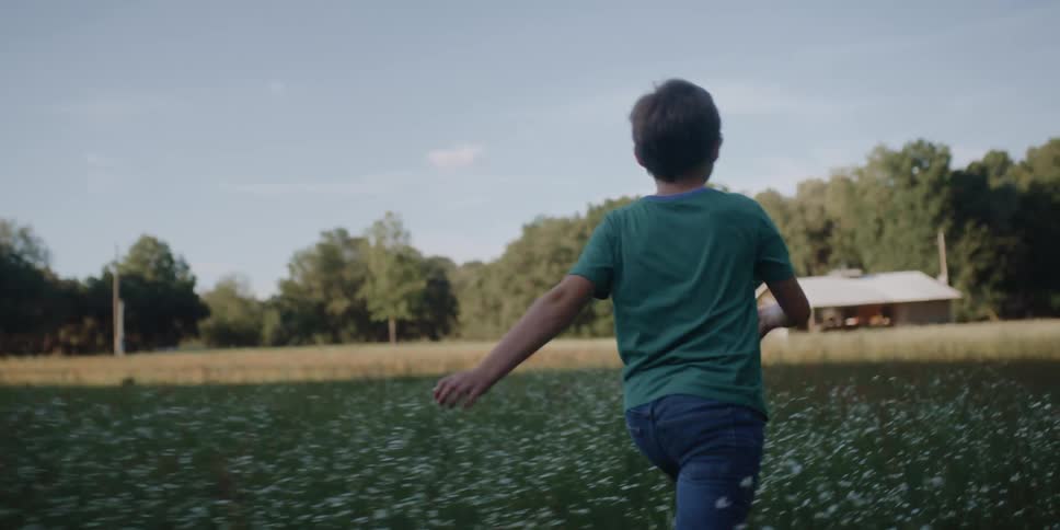 Boy with a green t shirt and shorts runs across the field with flowers