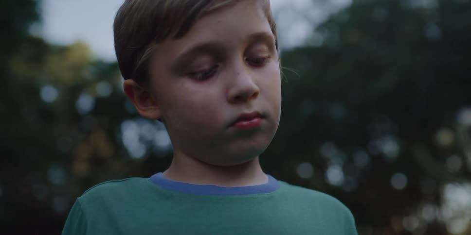 A young boy holds a wild flower and looks at it