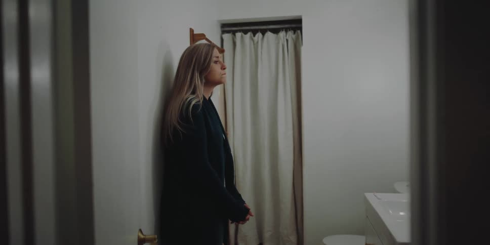 A young woman stands in a bathroom and fights back tears
