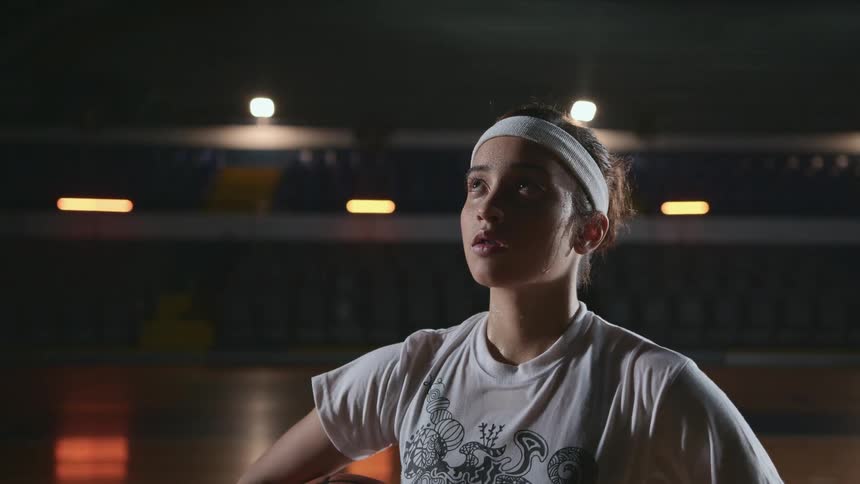 A girl is standing in a gym and holding a basketball