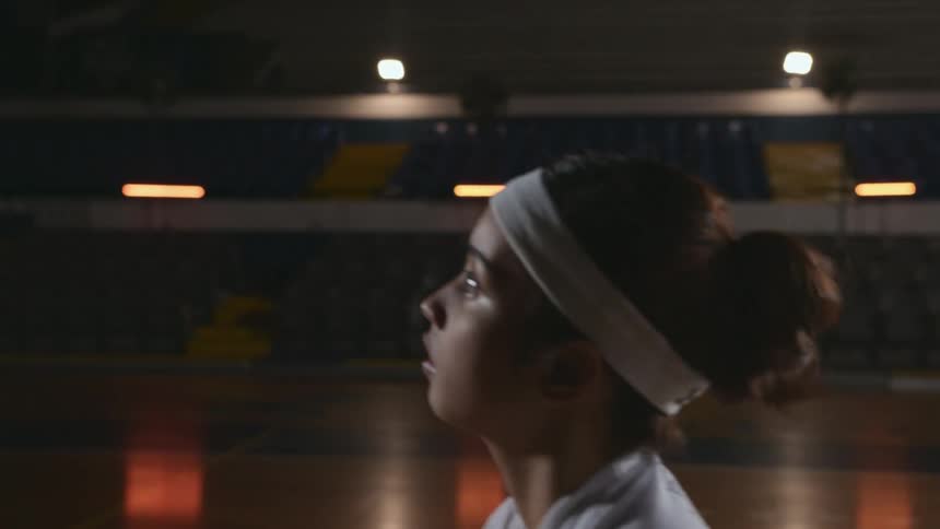 A teenage girl shoots baskets in a gymnasium