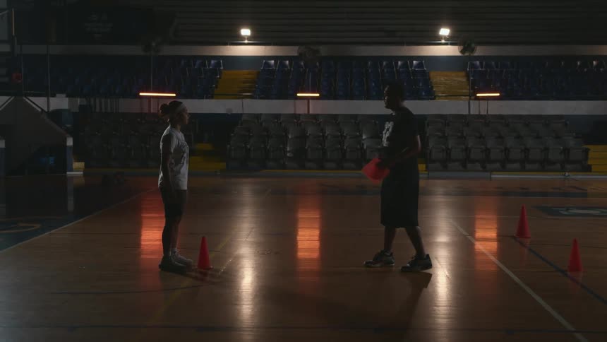 A man and a girl in a gym with cones on the floor and seats in the background