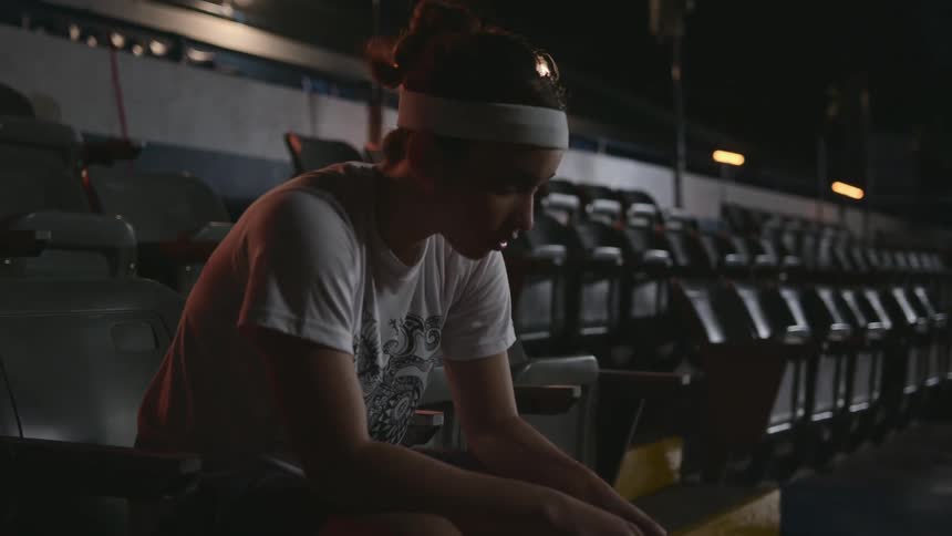 A teenage girl sits on a stadium chair and lowers her head