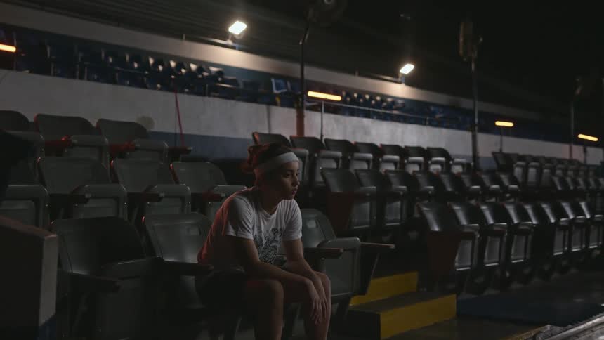 A woman sits alone in a stadium with her elbows resting on her knees