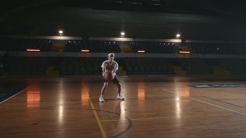 Teenage girl dribbling a basketball inside a dimly lit indoors court
