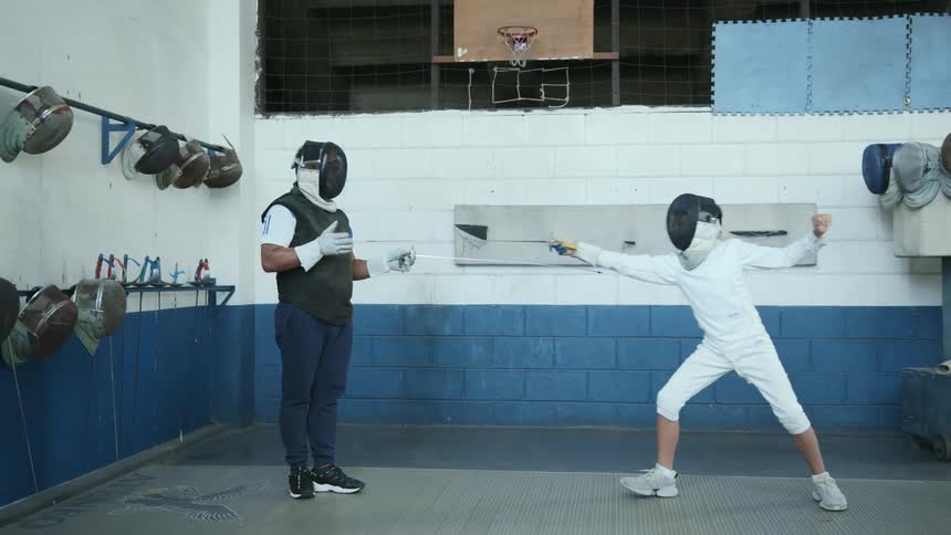 Two people in a room with fencing mask and swords practicing with a wall in the background