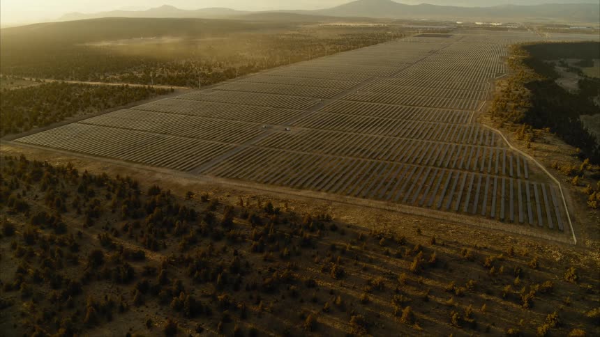 Wide overview of an immense solar farm located on an arid plateau with white data center buildings in the distance