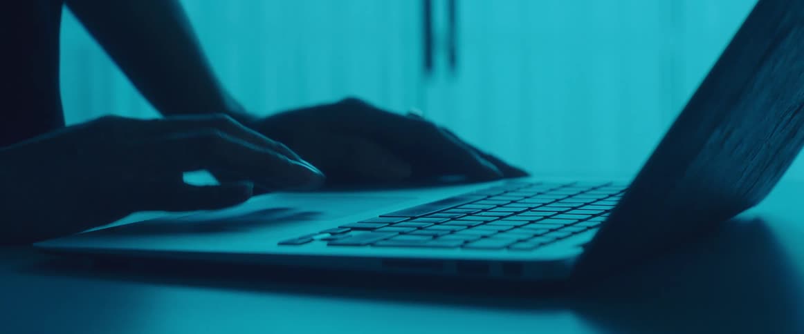 Hands typing on the keyboard of a laptop in side a dimly lit room