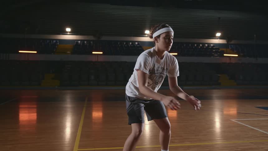A teenage girl dribbling and passing a basketball on a basketball court indoors