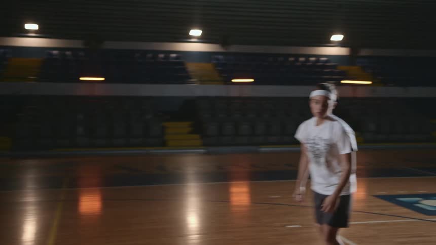 A teenage girl takes a practice shot with a basketball in a poorly lit gym