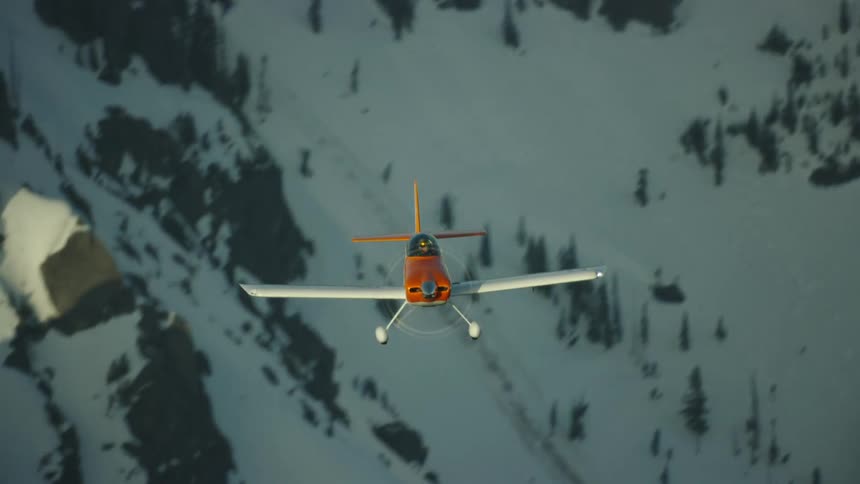 A white and orange acrobatic single engine airplane flies in straight and level flight towards the camera at sunset in high alpine mountains in winter
