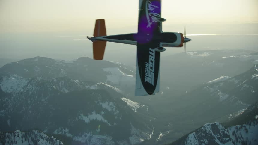 A single engine airplane breaks sharply left and dives out of frame towards the snow covered valley bleow