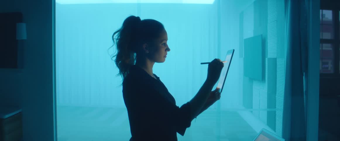 A woman standing inside of a room at home sketches on a tablet
