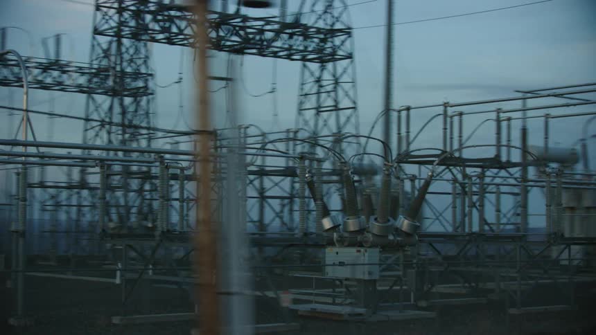 An electrical grid substation is seen as the camera rapidly rotates around communicating the energy needs of the world at sunset