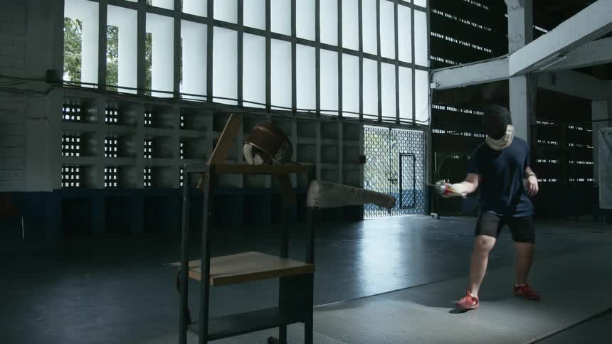 Young man wearing fencing hat practices with a dummy inside a gym